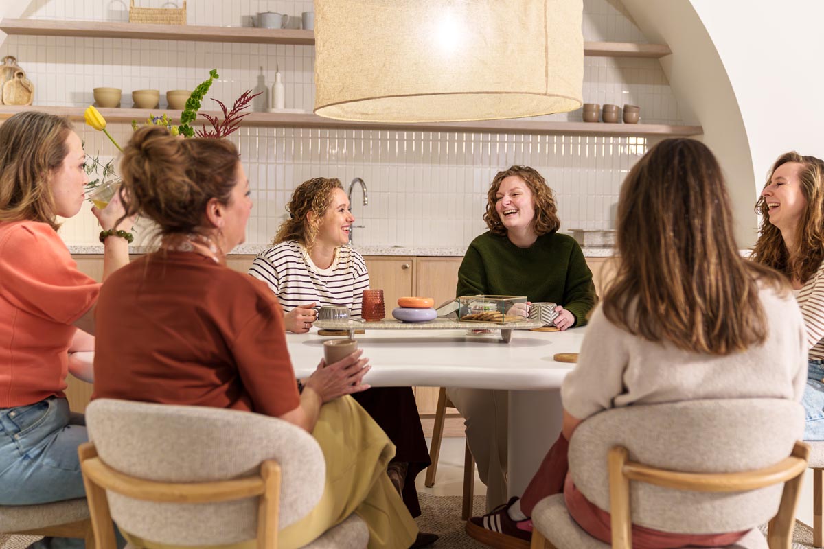 Zes medewerkers van Verloskundigenpraktijk Luna zitten lachend om tafel