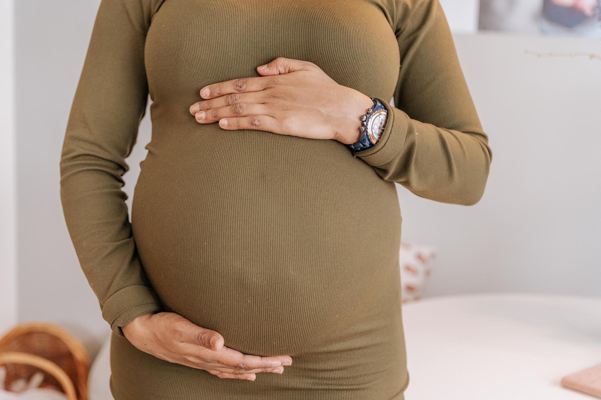 Vrouw in mosgroene jurk heeft haar handen bovenop en onder haar zwangere buik